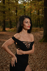 Beautiful woman wearing a long black dress posing in the woods on a sunny autumn afternoon.