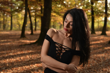 Beautiful woman wearing a long black dress posing in the woods on a sunny autumn afternoon.