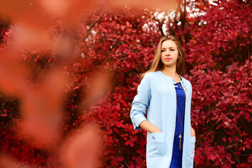 Business woman in a light coat in autumn park on the background of red foliage