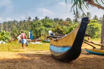 Tropical beach with palms and fishing boats in Mirissa, Sri Lanka with fisherman on the background