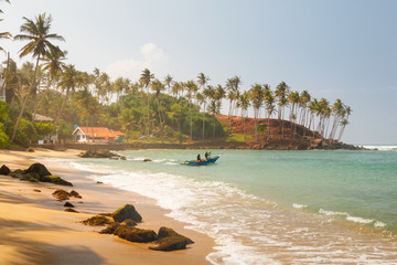 Coconut palm and sun lights through trees on beach with fishermen which is going to the water, Mirissa, Sri Lanka © Kennymax