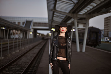 Obraz na płótnie Canvas Young sexy woman dressed in black posing on a train station pier.