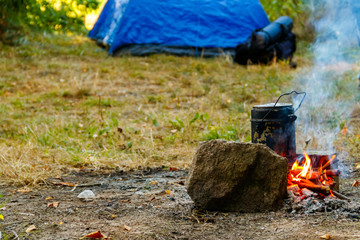 Cooking on campfire in camping. Tent and backpack on background