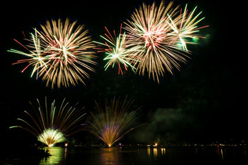 Colorful fireworks explosions in the night reflecting in water