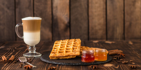fresh belgian waffles, tasty jam and latte coffee on a wooden background. top view.