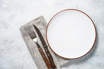 White plate and cutlery on stone table top view. 