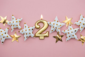 Number 2 gold candle and stars on a pastel pink background