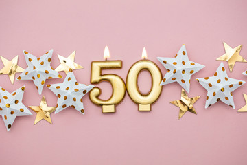 Number 50 gold candle and stars on a pastel pink background