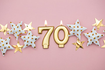 Number 70 gold candle and stars on a pastel pink background