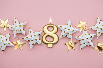 Number 8 gold candle and stars on a pastel pink background