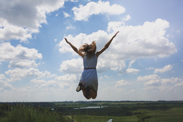 Young hipster girl is having fun in summer holidays. Woman in sunglasses is jumping high on the hill with a beautiful nature view. Freedom and travel lifestyle concept. Happy emotions and laugh.