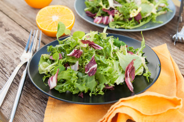 Fresh green salad with spinach, arugula, romaine and lettuce with orange fruit. Rustic wooden table. 