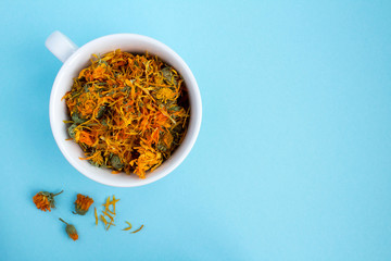 Dry calendula flowers in the white cup  on the blue background.Copy space.Top view.