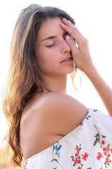 Portrait of a beautiful girl with bare shoulders and closed eyes gently touching her face and tilting her head towards the camera