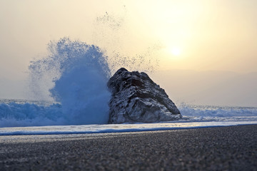 Sea wave beats on the rock against the sunset © photosaint