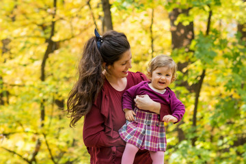 Fototapeta premium Happy Mother Hugging her Baby Girl in the Autumn Park .Mother and Daughter .Happy Family, Mother with Little Child in the Nature