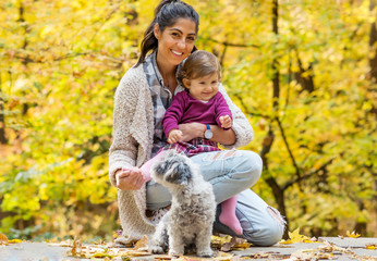 Fototapeta premium Happy Mother with her Baby Girl and her Dog in the Autumn Park .Mother and Daughter .Happy Family, Mother with Little Child and Dog in the Nature
