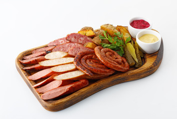 assorted sausages and meat with vegetables with mustard and ketchup on a wooden board isolated on white background