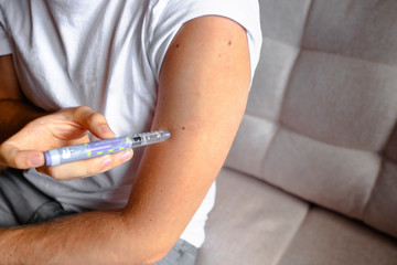 close up of handsome stylish young teen caucasian with syringe inject insulin to his shoulder himself at home .  Diabetes patient shot by syringe with dose, subcutaneous hand vaccination concept 