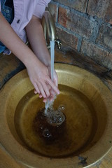 Girl washing her hands under water over a bronze sink
