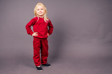 blonde blue-eyed little model girl in a red sports suit posing in the studio on a black background.active childhood full length portrait sporty costume hip-hop dancer