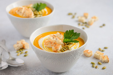 Pumpkin soup with cream, croutons, pumpkin seeds and parsley on a gray concrete or stone background, selective focus