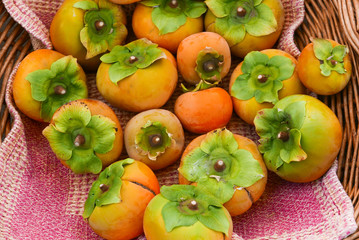 a basket of bright orange persimmons on a pink cloth