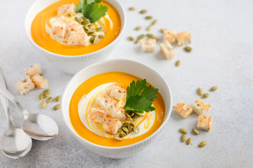 Pumpkin soup with cream, croutons, pumpkin seeds and parsley on a gray concrete or stone background, selective focus