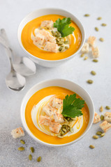 Pumpkin soup with cream, croutons, pumpkin seeds and parsley on a gray concrete or stone background, selective focus