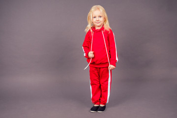 blonde blue-eyed little model girl in a red sports suit posing in the studio on a black background.active childhood full length portrait sporty costume