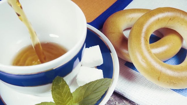 Slow motion pour tea into a beautiful white blue Cup on a saucer with sugar and mint near the bagels Baranka
