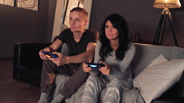 Couple playing videogame on console. Sitting on sofa at home. Girl wins.