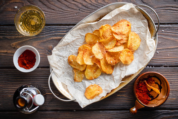 Homemade potato chips strewn with rock salt and paprika served with sous on a wooden rustic table with a bottle and glass of beer.