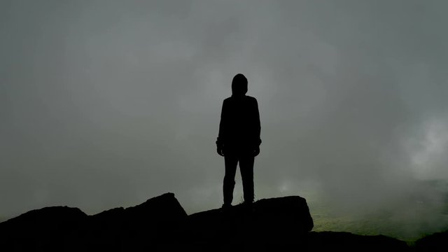 Mysterious silhouette of a man against the background of gray clouds (fog) high in the mountains.