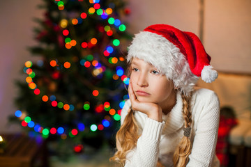 Sad girl near christmas tree at home