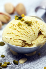 Pistachio ice cream scoop with chopped nuts and white chocolate on a rustic background.