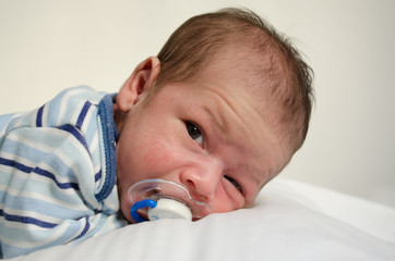 Newborn two weeks old baby boy laying down on white sheet awake