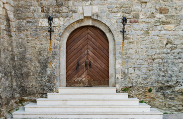 Fototapeta na wymiar Old wooden doors of an old castle with a white staircase and a stone wall.