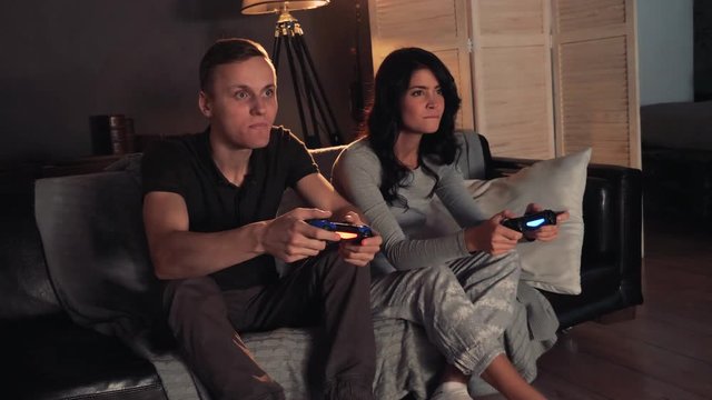 Couple playing videogame on console. Sitting on sofa at home. Men wins.
