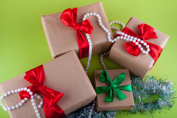 Holiday gifts in craft boxes with red, green bows on green background