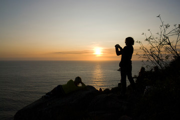 Eine Frau fotografiert den Sonnenuntergang am Meer / Woman photographs the sunset by the sea