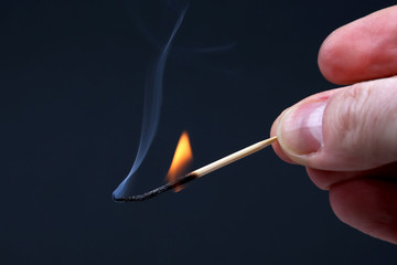Burning and Smoking wooden match in hand on dark background