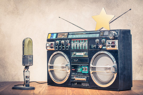 Retro old ghetto blaster stereo radio cassette tape recorder boombox from circa 1980s, large studio microphone and golden star front concrete wall background. Vintage instagram style filtered photo