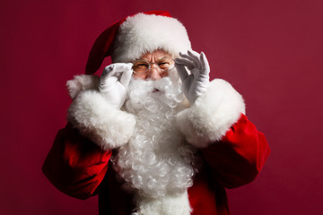 Portrait of man in Santa Clause costume wearing glasses while posing on red background, Christmas and New year concept