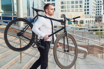 Handsome young businessman in a white shirt and black tie carries his bike