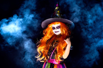 Beautiful girl in a witch costume on a dark background in smoke. Portrait of little girl in...