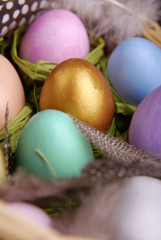 Wicker basket with colored Easter eggs, feathers, decorative chicken and a wish on a wooden label on a dark wooden background. Focus on the golden egg.