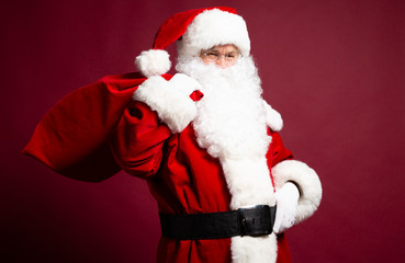 Portrait of grandfather in Santa Clause costume with gift sack on back posing on red background, Christmas and New year concept