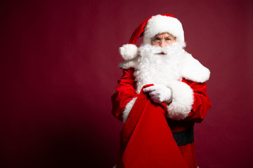 Portrait of grandfather in Santa Clause costume with gift sack on back posing on red background, Christmas and New year concept