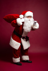 Portrait of grandfather in Santa Clause costume with gift sack on back posing on red background, Christmas and New year concept